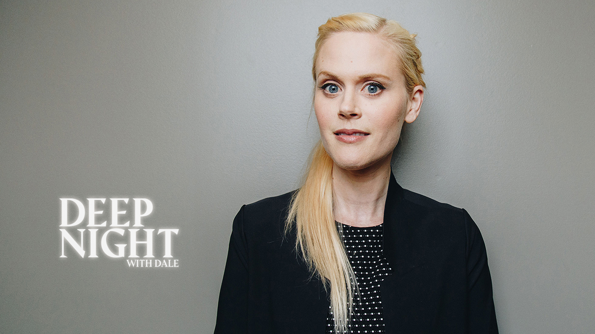 Photo of Janet Varney wearing black blazer over polka dot shirt against a gray background.